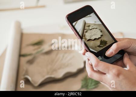 Foto di ceramiche fatte a mano in officina. Ceramica blog proprietario fare foto di lastra di argilla su smartphone lavorando in studio. Donna blogger artista Foto Stock