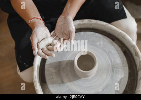 Potter mani sopra la rotella. Artista autonomo della ceramica nella modellatura creativa dello studio dalla tazza o dal vaso fatti a mano grezzi di argilla che modellano. Produzione ceramica Foto Stock