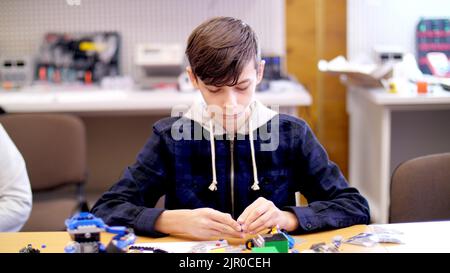 il ragazzo di 12 anni, gioca nel designer da cubi, piastre, circuiti, fili. un piccolo inventore crea robot, macchine da diverse parti del designer. Foto di alta qualità Foto Stock