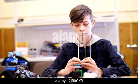 il ragazzo di 12 anni, gioca nel designer da cubi, piastre, circuiti, fili. un piccolo inventore crea robot, macchine da diverse parti del designer. Foto di alta qualità Foto Stock