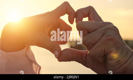 La coppia disabile fa il cuore con le mani alla luce del sole in primo piano Foto Stock