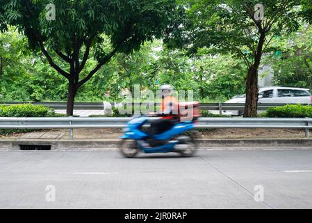 Corriere o addetto alla consegna in moto in movimento veloce, movimento sfocato. Il corriere effettua ordini di consegna nell'area verde urbana. Foto Stock