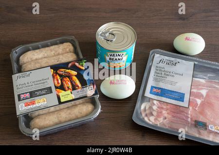 Ingredienti per cucinare una tradizionale colazione inglese in cucina - uova, pancetta, salsicce e fagioli al forno Heinz. REGNO UNITO. Concetto - alimentazione non sana Foto Stock