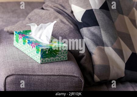 Un ritratto di una scatola colorata di fazzoletti di carta in piedi sul lato di un divano in un salotto pronto per essere utilizzato quando basta soffiare il naso, Foto Stock