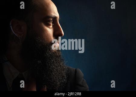 Ritrattistica del profilo di un uomo barbuto che guarda alla luce. giovane uomo sofisticato che indossa un abito che guarda direttamente alla luce. Foto Stock