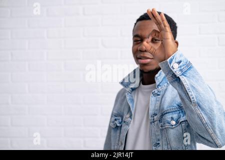 Ritratto giovane bel nero africano uomo mostrando ok gesto indossare jeans giacca denim contro mattone con parete all'aperto con copyspace. Foto Stock