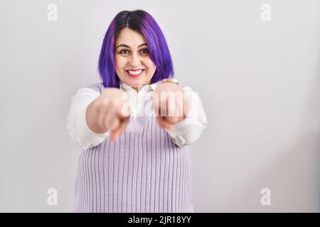 Più dimensione donna wit capelli viola in piedi su sfondo bianco puntando a voi e la fotocamera con le dita, sorridendo positivo e allegro Foto Stock