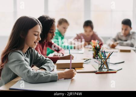 Scuola di scrittura saggio durante la lezione con i bambini misti in classe Foto Stock