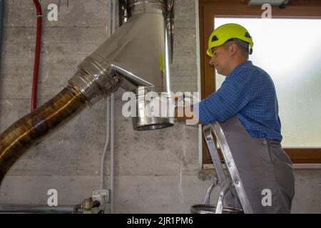 Immagine di un idraulico a mano duro su una scala che ripara e monta un tubo in acciaio inossidabile di una canna fumaria della caldaia. Fai da te il lavoro. Foto Stock