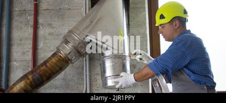 Immagine di un idraulico a mano duro su una scala che ripara e monta un tubo in acciaio inossidabile di una canna fumaria della caldaia. Fai da te il lavoro. Banner Foto Stock