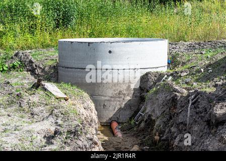 Serbatoio settico in calcestruzzo composto da diversi anelli con tubo di scarico arancione sul fondo. Foto Stock