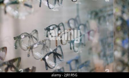Primo piano, vetrina nel negozio ottico, ottica, negozio di optician, negozio di occhiali, un sacco di occhiali, montature, mano dell'uomo sceglie occhiali correttivi alla moda, occhiali . Foto di alta qualità Foto Stock