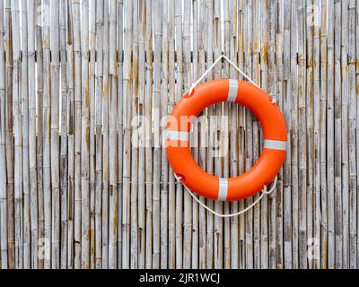 Un anello di sicurezza arancione salvagente appeso sullo sfondo della parete di bambù recinzione con spazio copia. Attrezzatura di salvataggio. Lifesaver, concetti di sicurezza. Foto Stock