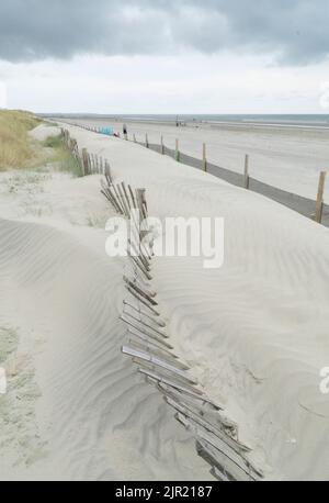 West Wittering, Regno Unito, 21 agosto 2022: La sabbia si accumula alla base delle dune di sabbia di West Wittering e sopraffa una vecchia recinzione di legno. Nuova rete in plastica Foto Stock