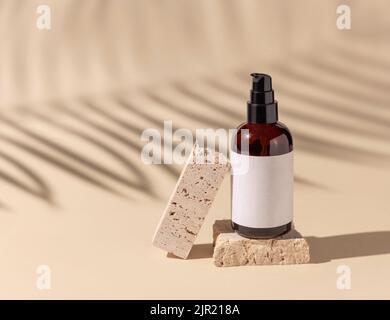 Marrone vetro cosmetico una bottiglia di pompetta su travertino in pietra su beige chiaro. Palm foglia ombre dure, primo piano, etichetta mockup. Prodotti di bellezza per la cura della pelle, loti Foto Stock