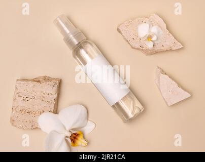 Spruzzatore bottiglia vicino fiori di orchidea bianca e pietre beige sulla vista dall'alto beige chiaro, mockup. Pacchetto prodotti di bellezza per la cura della pelle. Cosmetici naturali, Foto Stock