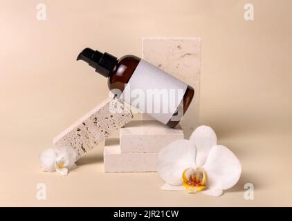 Vetro scuro una bottiglia cosmetica pompa con etichetta vuota vicino a fiori di orchidea bianca e pietre su giallo chiaro, primo piano, mockup. Bellezza artigianale per la cura della pelle Foto Stock
