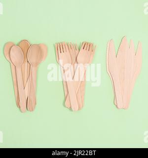Forchette, coltelli e cucchiai in legno senza scarti su fondo verde pastello. Giacitura piatta Foto Stock