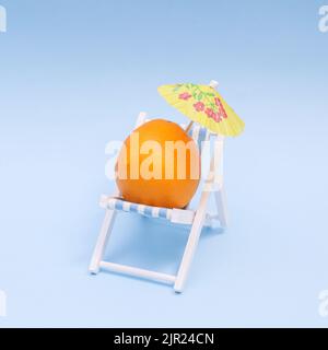 Concetto estivo con arancio e ombrellone su sdraio su sfondo blu. Concetto creativo Foto Stock