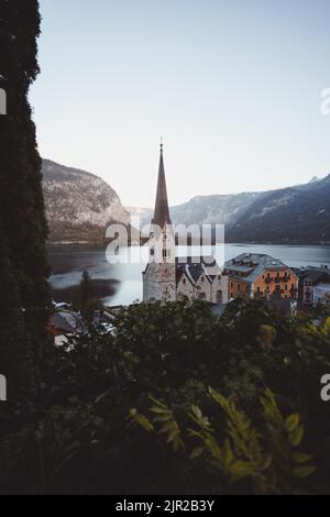 Una foto verticale della Chiesa luterana di Hallstatt con alberi e un lago sullo sfondo Foto Stock