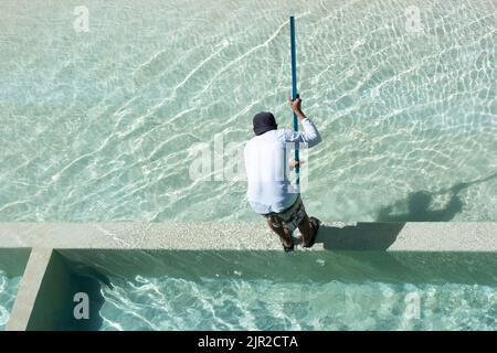 Ripresa dall'alto di un addetto alla manutenzione che pulisce una piscina con una spazzola in Messico Foto Stock