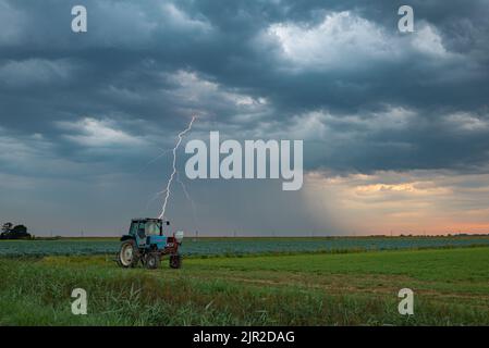 Un fulmine colpisce giù da un cielo drammatico tempesta dietro un trattore in campagna Foto Stock