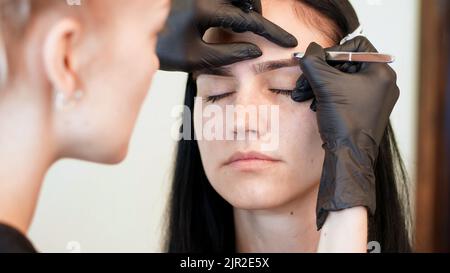 salone di bellezza. primo piano, le mani del cosmetico in guanti di gomma nera tengono le pinzette e tirano fuori le sopracciglia. Master corregge la forma delle sopracciglia. Foto di alta qualità Foto Stock