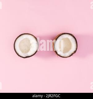 Una noce di cocco spezzata in due peaces su sfondo rosa pastello. Giacitura piatta Foto Stock