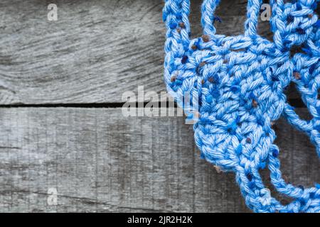 dettaglio di un tappeto blu con forme a cuore per il pavimento, accovacciato a mano, su sfondo grigio in legno. angolo di una tovaglia posta sul pavimento Foto Stock