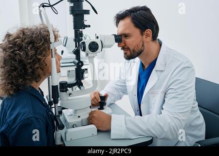 L'optometrista maschile che esegue il test della vista per il bambino maschio presso la clinica oftalmologica moderna. Esame oculare e diagnosi visiva per bambini Foto Stock