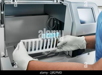 Tecnico di laboratorio che carica i campioni di sangue per l'analisi del test della coagulazione in un analizzatore automatico della coagulazione, primo piano. Analisi della coagulazione dei campioni di sangue Foto Stock