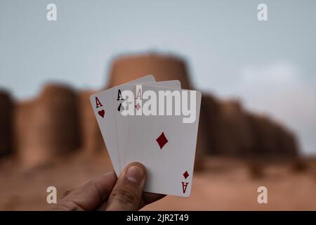 Un primo piano di una mano che tiene tre assi sullo sfondo del forte Derawar in Pakistan Foto Stock