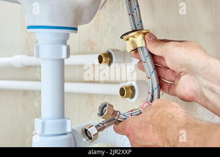 Rubinetto collegato al lavello utilizzando tubi flessibili dell'acqua intrecciati e all'alimentazione idrica domestica durante i lavori idraulici. Foto Stock