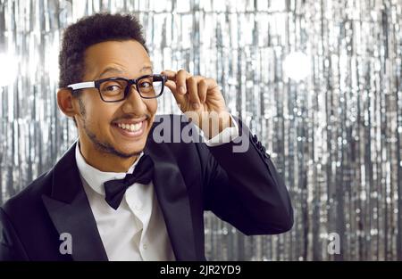 Felice bel giovane uomo nero in abito elegante e occhiali guardando la fotocamera e sorridendo Foto Stock