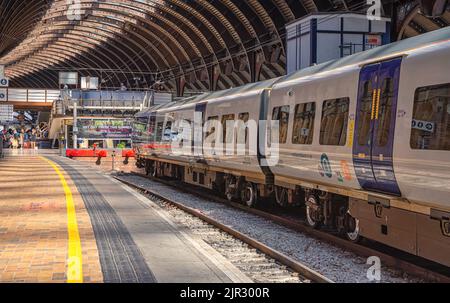 Accanto alla piattaforma della stazione ferroviaria si trova un treno. Ci sono passeggeri sullo sfondo e alcuni camminano attraverso un ponte pedonale. Una storica tettoia curva è Foto Stock