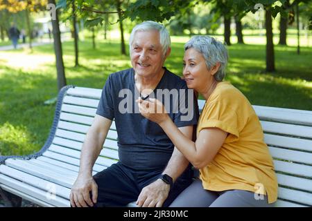 Abbastanza multi razziale anziani 60s coppia che riposa sedersi sulla panca nel parco dopo una passeggiata, mattina a piedi sorridendo godere parlare rilassarsi all'aperto discutere qualcuno. Montare f Foto Stock