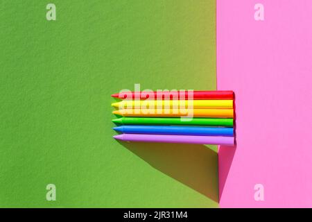 Concetto creativo di ritorno a scuola. Diversi pastelli colorati in cera isolati sullo sfondo rosa e verde. Spazio di copia. Foto Stock