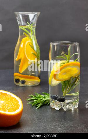 Mezza arancia e rametto di rosmarino sul tavolo. Acqua infusa di arancia in vetro e bottiglia. Vista dall'alto. Sfondo nero. Foto Stock