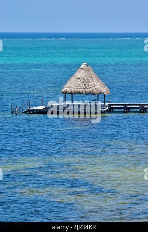 Un palapa alla fine di un molo contro le acque blu turchesi di San Pedro, Belize, America Centrale. La barriera corallina e il Mar dei Caraibi sono lontani. Foto Stock