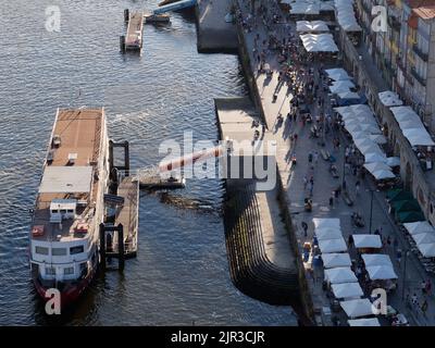 Ribeira distretto di Porto Portogallo dall'alto con una barca ormeggiata sul fiume douro. La gente cammina lungo la passeggiata tra le bancarelle del mercato. Foto Stock