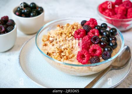 Farina d'avena per primo piano con diversi frutti di bosco e noci tritate in un recipiente di vetro. Cibo sano ed equilibrato Foto Stock