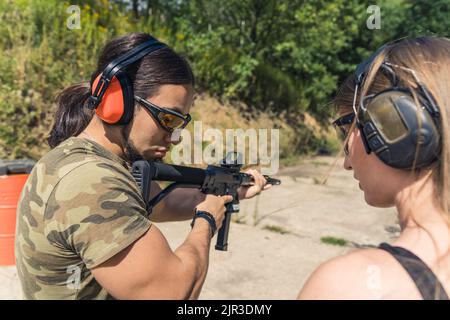 Uomo e donna bianchi in occhiali di protezione e cuffie all'esterno campo di tiro allenamenti con mitragliatrice. Allenamento con armi da fuoco, tiro orizzontale all'aperto. Foto di alta qualità Foto Stock