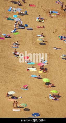 Uno scatto verticale della spiaggia di Laga in Spagna con la gente che fa il bagno e che si distensione sulla spiaggia, scatto aereo Foto Stock