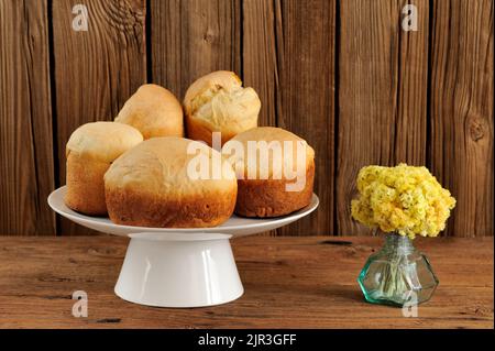 Paska, pani dolci pasquali dell'Europa orientale su piedistallo bianco con fiori gialli su sfondo di legno orizzontale con spazio Foto Stock
