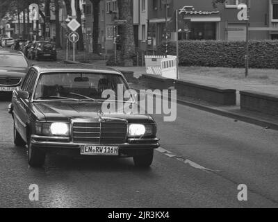 Una foto in scala di grigi di una Mercedes Classe S classica che naviga per le strade di Bochum in una giornata di pioggia Foto Stock