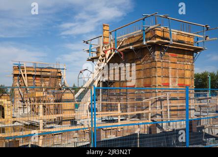 Il calcestruzzo viene gettato nel cantiere di edifici commerciali circondato da una recinzione di sicurezza blu. Foto Stock