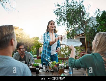 Perchè Grazie. un giovane gruppo di amici che gustano un pasto insieme mentre si siedono fuori intorno ad un tavolo in un giardino. Foto Stock