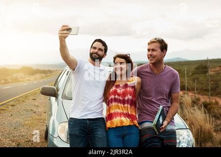 Scatta la nostra prima foto insieme per il viaggio: Un gruppo di giovani amici che si avvicinano o una foto autoritratto mentre si è in piedi accanto a una strada. Foto Stock