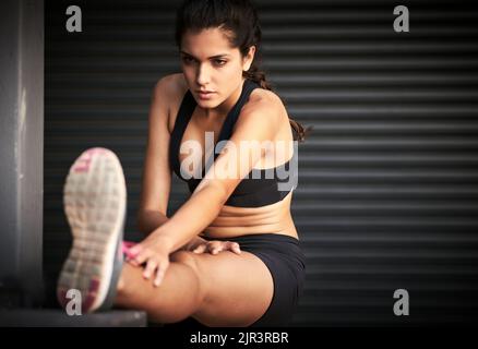 Im andare a dare il mio tutto. Una giovane donna attraente in piedi e stretching le gambe all'interno di un magazzino. Foto Stock