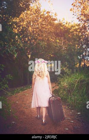 Ive ha tutto quello di cui ho bisogno. Una bambina irriconoscibile che cammina con una valigia su una strada sterrata fuori dalla natura. Foto Stock